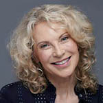 Headshot of a smiling white woman with blonde curly hair wearing a navy blouse.