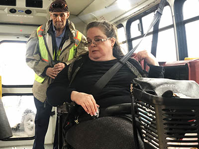 A man in a reflective vest listens to a woman in a motorized vehicle that is secured inside a van.