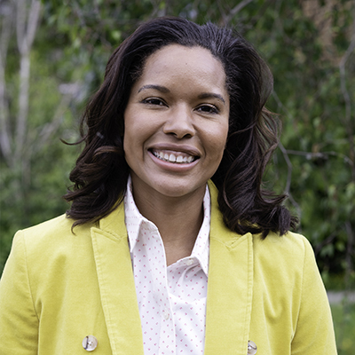 Outdoors portrait of a Black Latina woman wearing a bright yellow blazer.