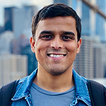 Headshot of a smiling man with brown hair, wearing a blue collared shirt, with the Seattle skyline behind him.