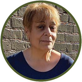 Circular photo with a forest-green frame of a Black woman with reddish-brown short hair wearing a darkish top, standing in front of a brick wall.