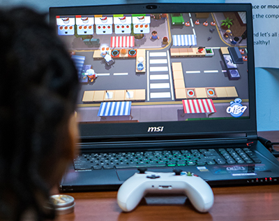 A close up of a computer screen on a laptop seen over the shoulder of a child whose head can be seen out of focus in the foreground.