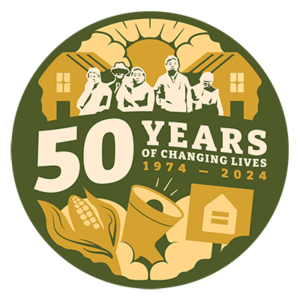 Circular dark green, peach and ivory graphic. It has silhouettes of several people in front of a pair of houses. The sun is shining from between two clouds. Text reads "50 years of changing lives, 1974-2024." Under the words are illustrations of an ear of corn, a megaphone, and a protest sign showing an equals symbol inside the outline of a house.