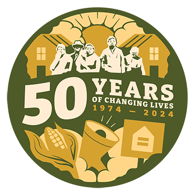 Circular dark green, peach and ivory graphic. It has silhouettes of several people in front of a pair of houses. The sun is shining from between two clouds. Text reads "50 years of changing lives, 1974-2024." Under the words are illustrations of an ear of corn, a megaphone, and a protest sign showing an equals symbol inside the outline of a house.