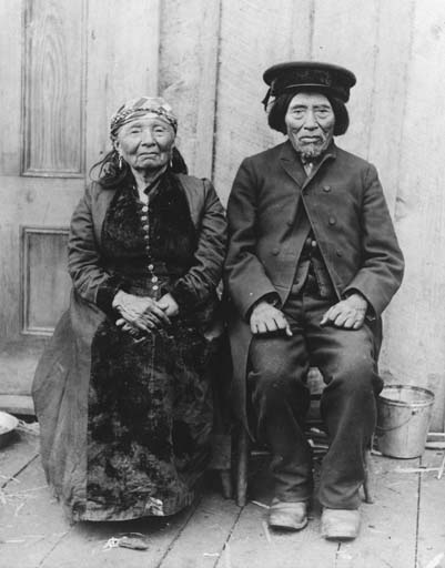 A black-and-white photo of an old man and woman sitting side by side.