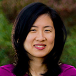 Headshot of an Asian woman wearing a fuschia top, in a outdoor setting.