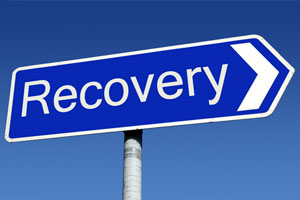 Blue road sign in the shape of an arrow that says "Recovery" in white letters