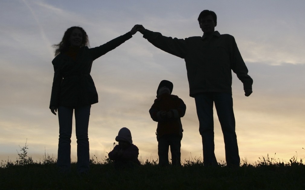 silhouette of a family with two adults forming a roof over the heads of two children at sunset