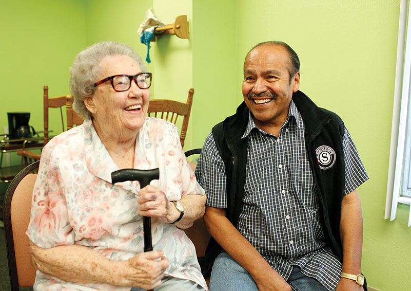 Elderly lady with cane sitting next to Senior Volunteer.
