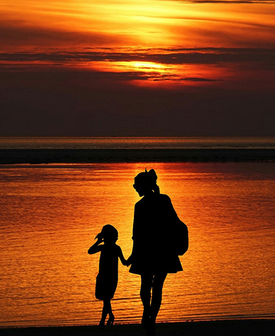 Silhouette of a mother & daughter holding hands in front of a brilliant orange sunset