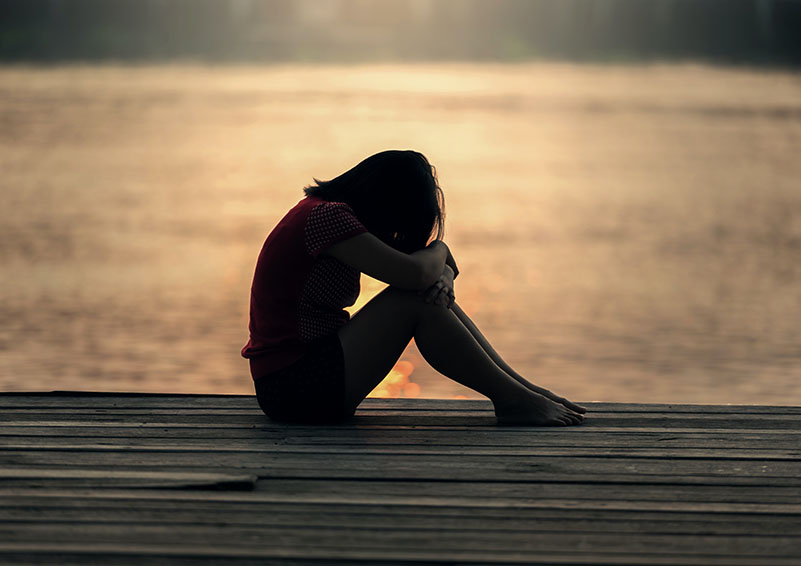 Silhouette of a sad teen girl sitting on a pier