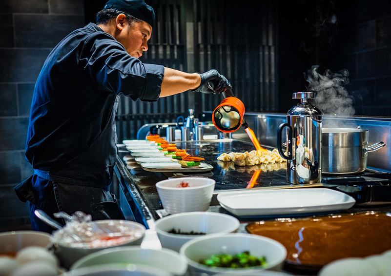 A chef dress in blue pours sauce on dumplings