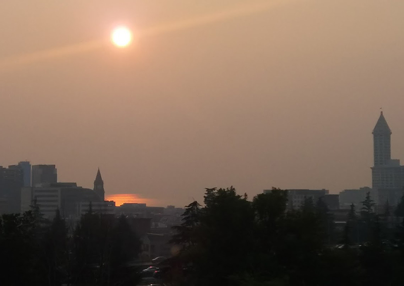 Seattle skyline through an orange-grey haze of wildfire smoke, with an orange sun above
