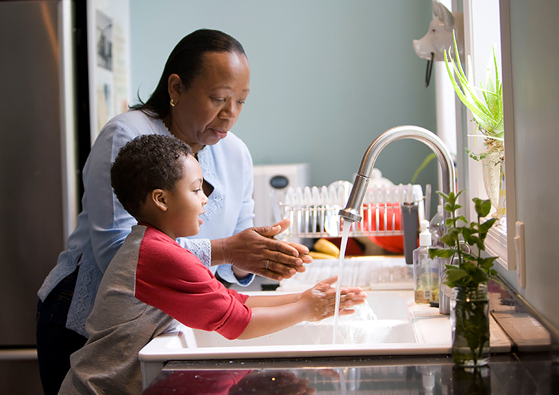 Mother & son wash hands at kitchen sink, plants in windowsill