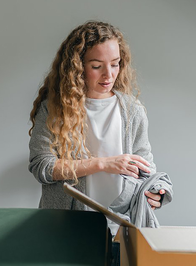 Woman with long blonde hair and a grey sweatshirt packs a moving box with belongings