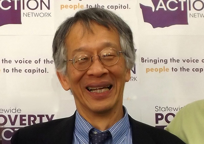 Headshot of an Asian man with greying hair and wire-rimmed glasses, grinning into the camera