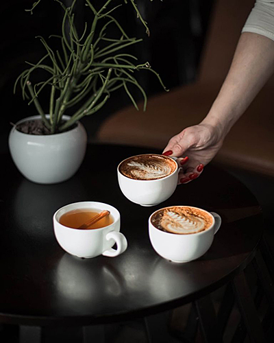 an arm reaching out to a small black table with three lattes in white mugs