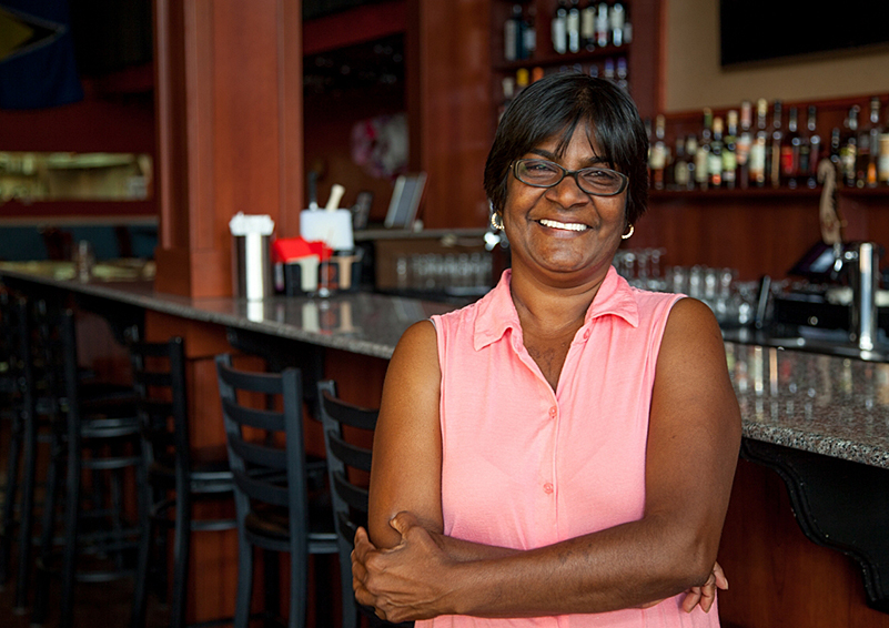 A Black woman restaurant owner smiles in front of a bar