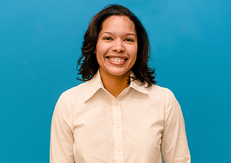Portrait headshot of woman in a white button-down shirt with blue background.