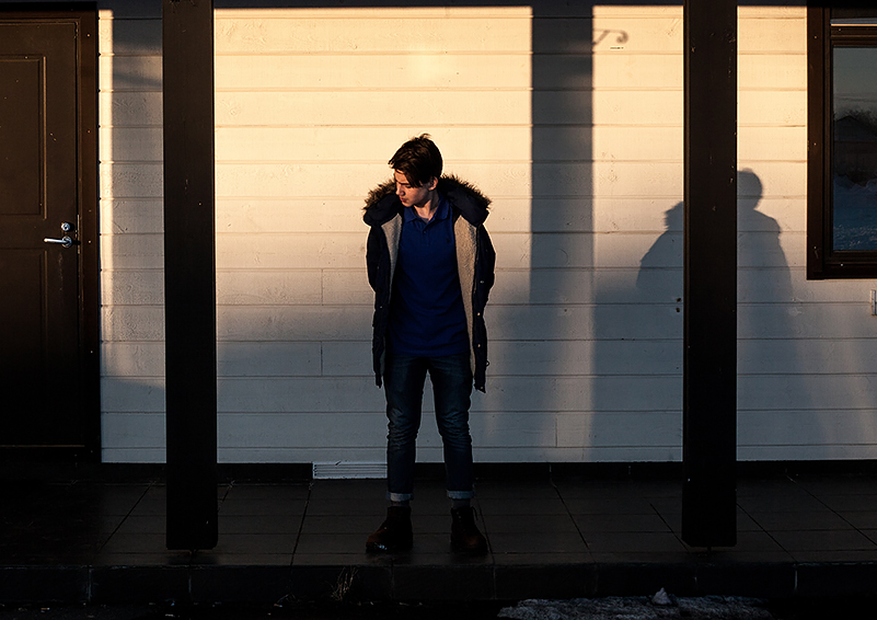 Young man in a hooded winter jacket and boots outside a building in the cold