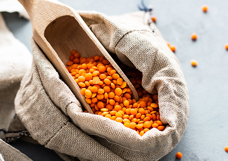 dried red lentils in a wooden scoop on top of a burlap bag
