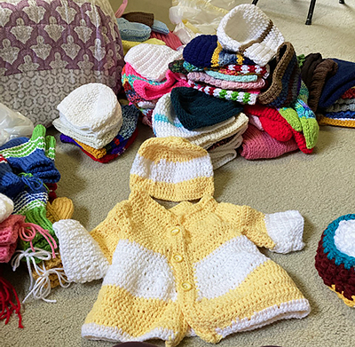 colorful knitted items on a beige rug with the corner of a quilted bed showing