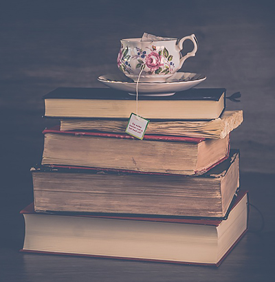 Stack of vintage hard-bound books with a flowery china teacup on top