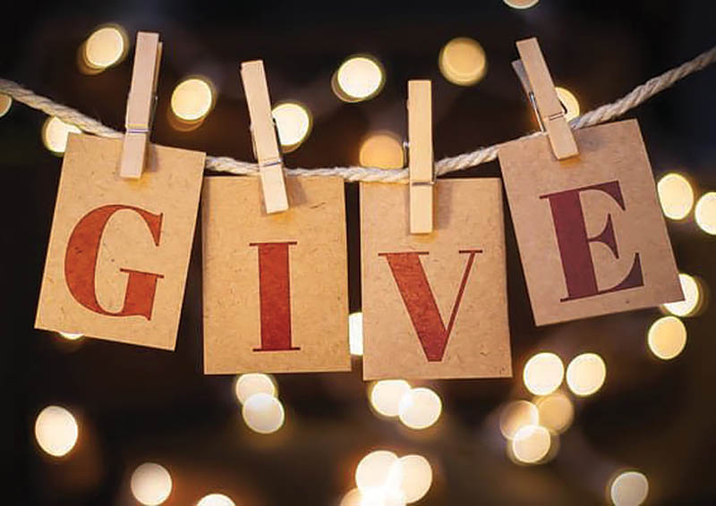 Photo of red capital letters G, I, V, and E on separate pieces of paper, clipped to a clothesline with clothespins on a black background with the glow of strings of lights