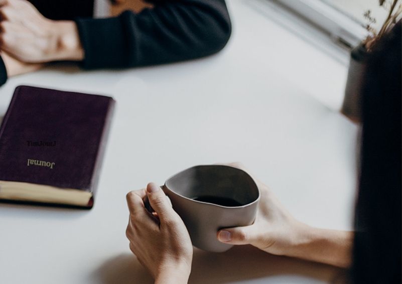 A close up of the hands of two people talking over coffee