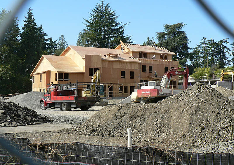 Large apartment complex under construction with unfinished exterior, with a large pile of gravel and big machinery in front of it