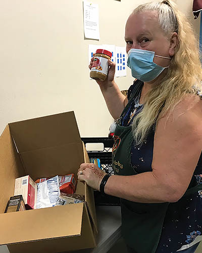 Woman with long blonde hair in a mask and apron boxes food in a food pantry