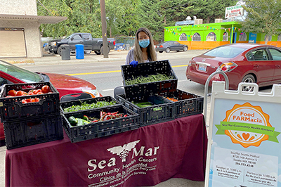 A woman stands behind a table with several crates of fresh vegetables