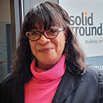 Headshot of a Black woman with glasses, wearing a hot pink turtleneck and black blazer