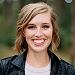 Headshot of a white woman with blonde hair, wearing a white shirt and black leather jacket