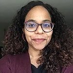 Headshot of a BlHeadshot of a Black woman with glasses and curly shoulder-length hair, wearing a purple top