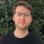 Headshot of a white man with glasses, wearing a black T-shirt