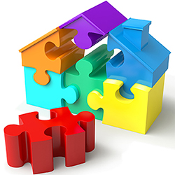 House made of bright puzzle pieces (purple, orange, blue, aqua, green and yellow) with one missing piece, a red one, in the foreground