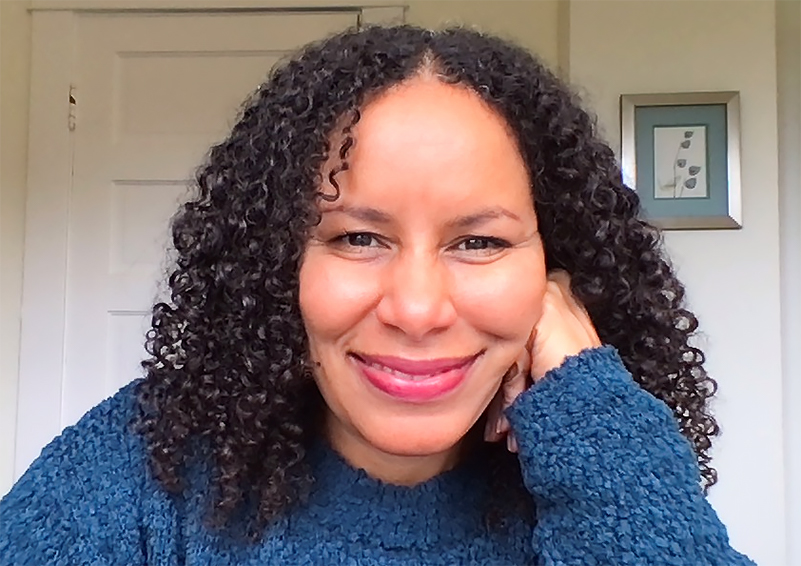 A smiling woman with curly hair wearing a blue sweater.