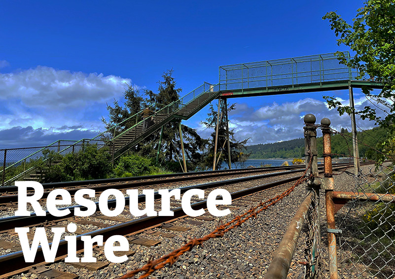 A pedestrian food bridge over train tracks along the coast, with the works "Resource Wire" embossed over it