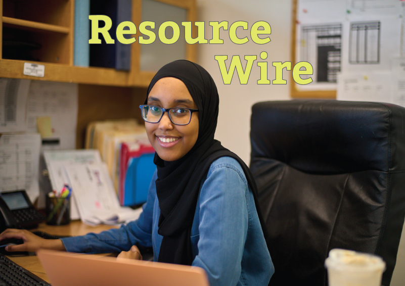 A woman in a black headscarf works on a computer at a desk