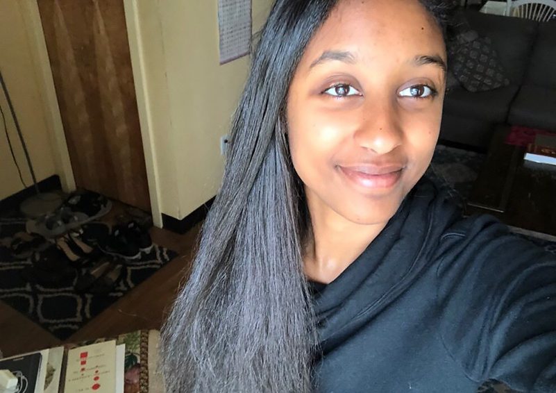 A smiling young women with dark hair in a dark hoodie looking off screen