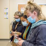 Three women wearing jackets and face masks count fake money.