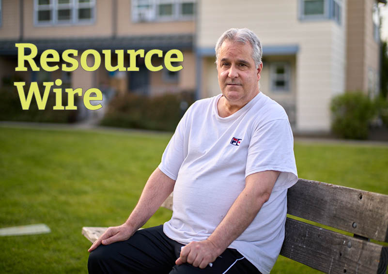 A man in a white t-shirt and black pants sits on a bench with a bright green lawn and buildings in the background. The words "Resource Wire" appear above him.