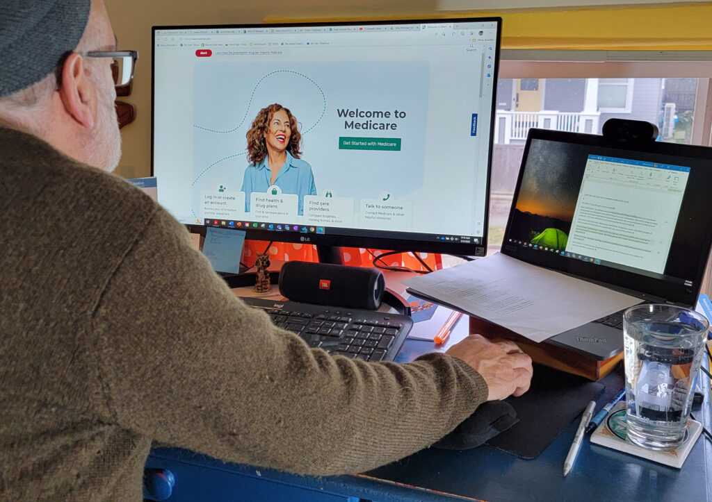 The author, Mike Buchman, looks at a computer screen that is open to a webpage that reads "Welcome to Medicare."