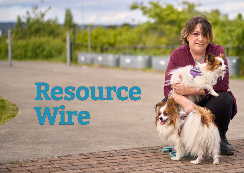 A woman wearing a cranberry-colored sweater crouches down a small dog on her lap and another infront of her. The words "Resource Wire" appear besides her.