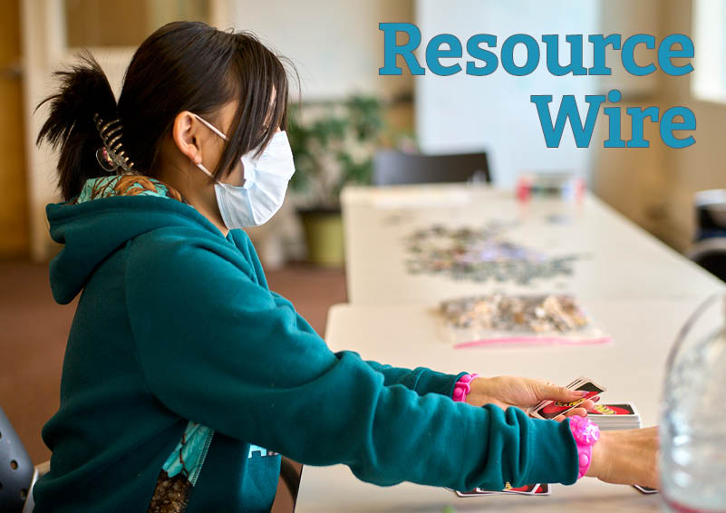A young girl with a pony tail and turquoise hoodies sits at a table an plays the card game UNO. The words "resource wire" appear beside her.