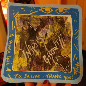 A painting of a splotchy gold-and-black square with a think blue border. The words "inspired growth" is etched in gold across a black patch.