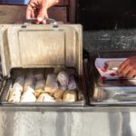 A close-up shot of a tamales wrapped in paper and tucked into a metal heating basket.