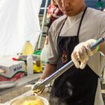 A young man strains ramen noodles fresh from a boiling pot of water.