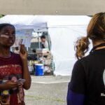 A young woman with a Bandaid on her cheek giver her order to an employee.